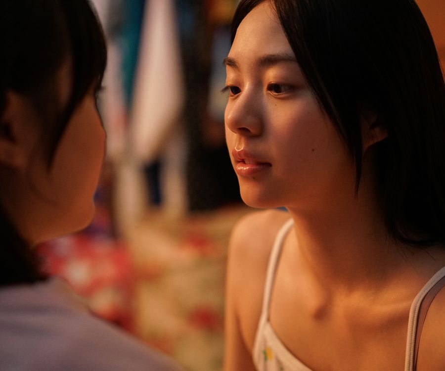 Two girls sitting on a bed, looking at each other