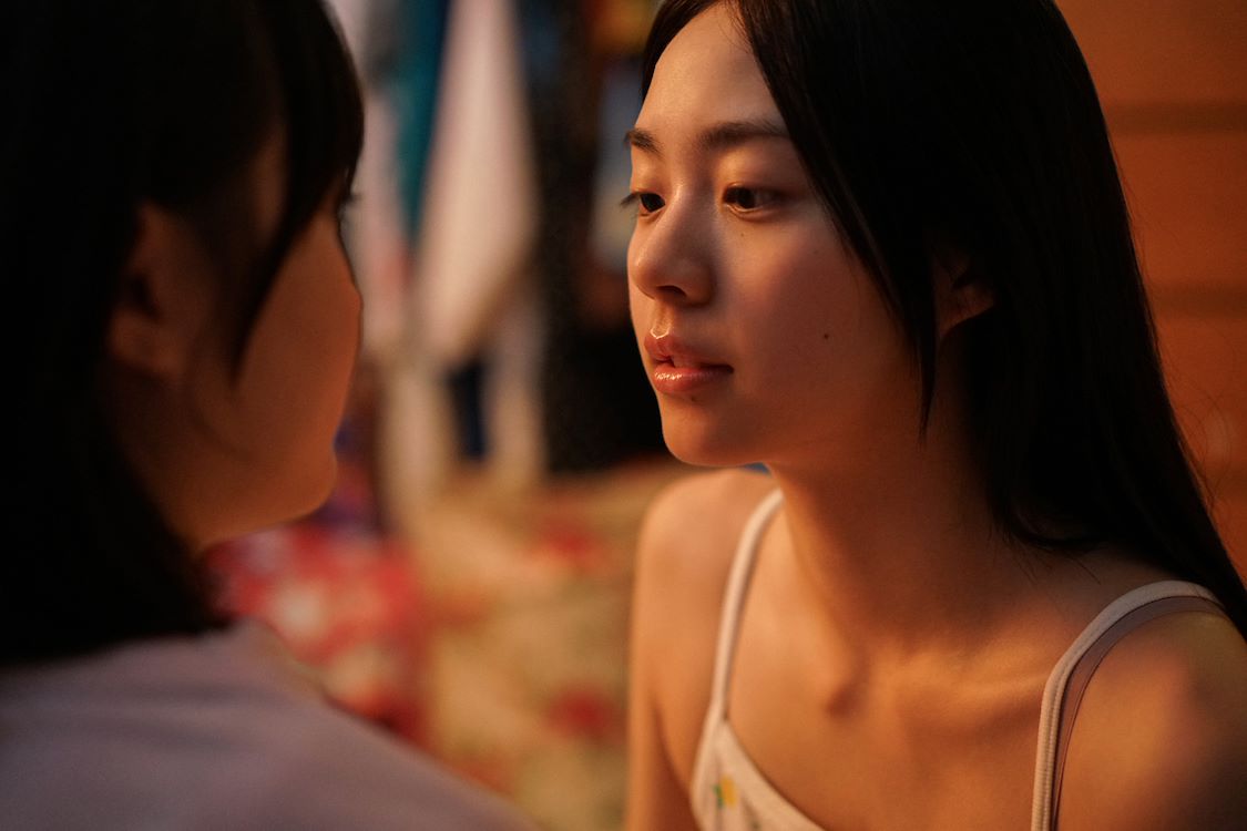 Two girls sitting on a bed, looking at each other