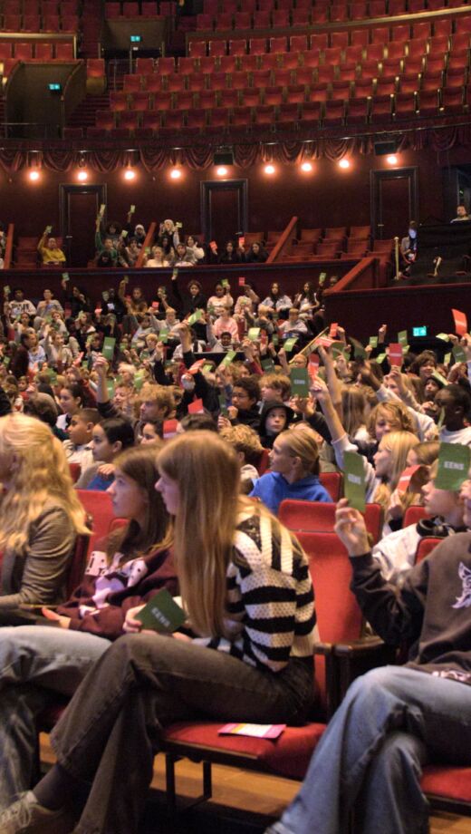 Middelbare scholieren in een theaterzaal houden kaartjes met 'eens' en 'oneens' omhoog