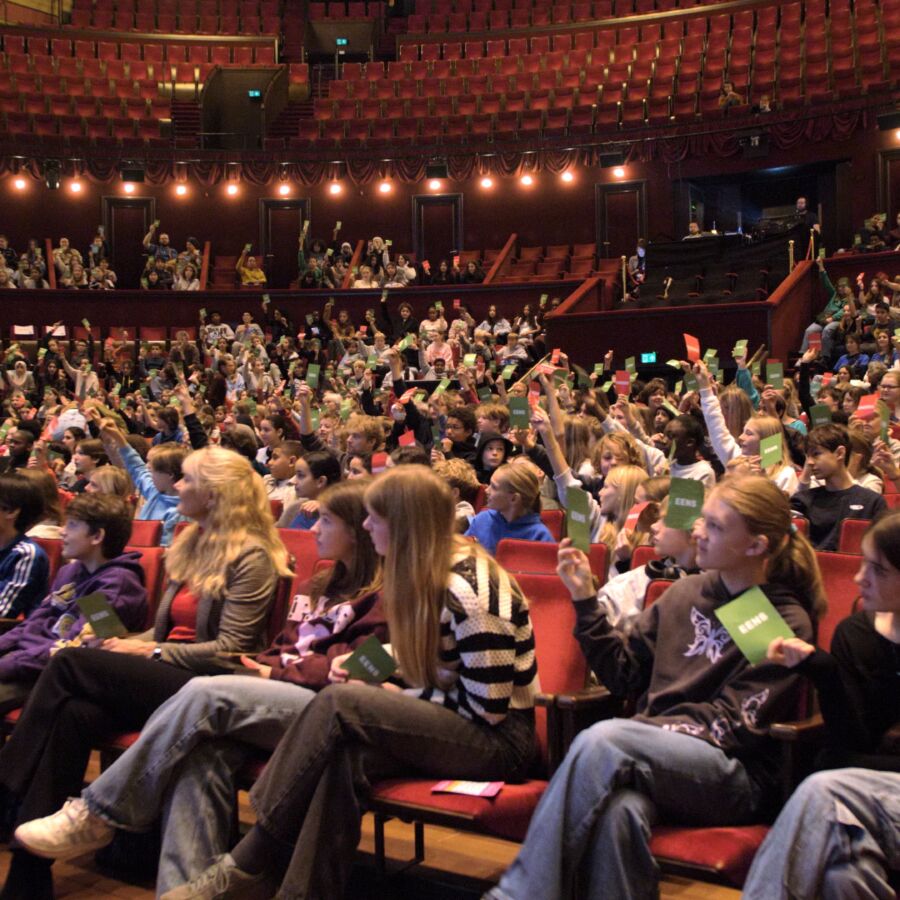 Middelbare scholieren in een theaterzaal houden kaartjes met 'eens' en 'oneens' omhoog