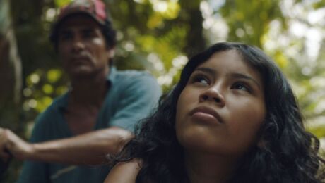 A young girl in the Amazon rainforest looks up at the sky.