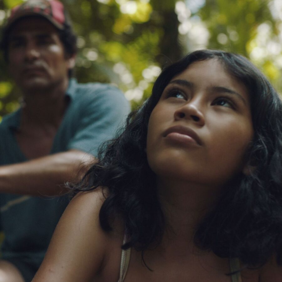 A young girl in the Amazon rainforest looks up at the sky.