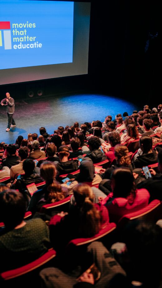 Een moderator staat in een bioscoopzaal voor een groep leerlingen