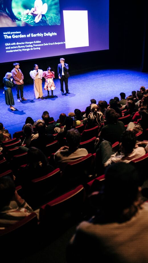 De cast van The Garden of Earthly Delights staat voor het scherm in een volle bioscoopzaal.