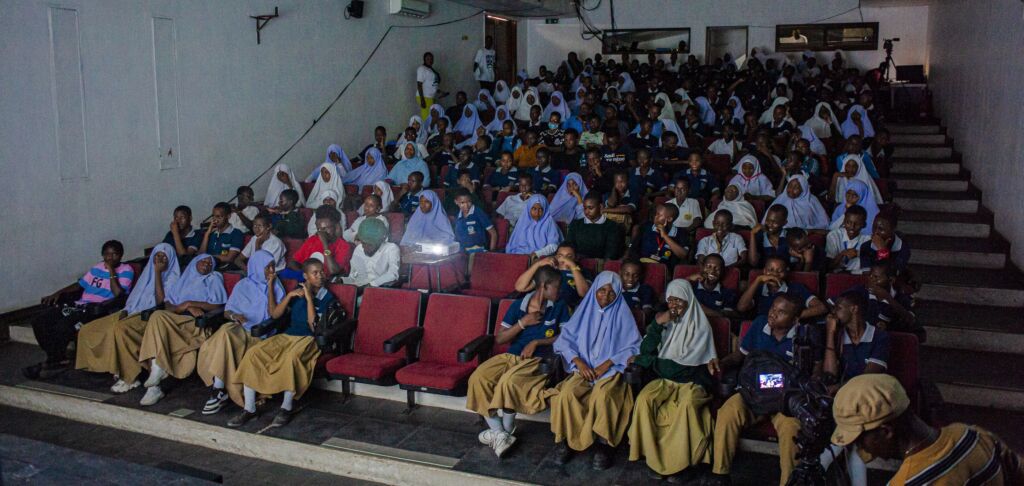 Screening room with boys in blue shirts and yellow pants and girls wearing light blue head scarfs.